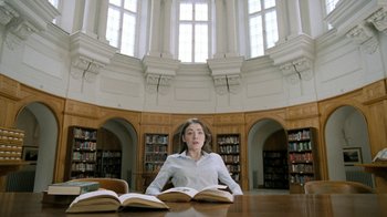 Movie still from “The Moth Diaries” (2011), directed by Mary Harron – A woman sitting at a table in front of two open books; Medium shot, Low angle