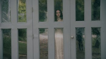 Movie still from “The Moth Diaries” (2011), directed by Mary Harron – A woman standing behind a glass door looking out at the camera; Wide shot, Over the shoulder angle