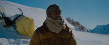 Movie still from “The Mountain Between Us” (2017), directed by Hany Abu-Assad – A man wearing a hat and a scarf on top of a snow covered slope; Medium shot, Low angle