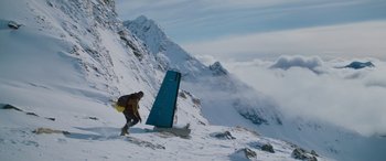 Movie still from “The Mountain Between Us” (2017), directed by Hany Abu-Assad – A man with a snowboard in the snow near a mountain; Extreme Wide shot, Low angle