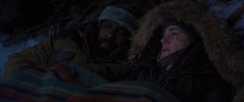 Movie still from “The Mountain Between Us” (2017), directed by Hany Abu-Assad – A man and a woman laying in the snow; Medium shot, High angle