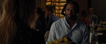 Movie still from “The Mountain Between Us” (2017), directed by Hany Abu-Assad – A man sitting at a table in front of other people; Close Up shot, Over the shoulder angle