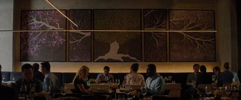 Movie still from “The Mountain Between Us” (2017), directed by Hany Abu-Assad – A group of people sitting at a table in front of a painting; Wide shot, Overhead angle