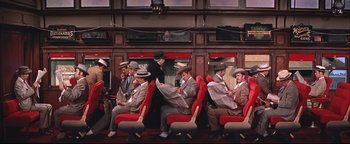 Movie still from “The Music Man” (1962), directed by Morton DaCosta – A group of men sitting on red seats on a train; Wide shot, High angle