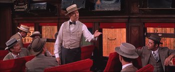 Movie still from “The Music Man” (1962), directed by Morton DaCosta – A man in a hat and a vest standing next to another man in a hat and a vest; Medium shot, Over the shoulder angle