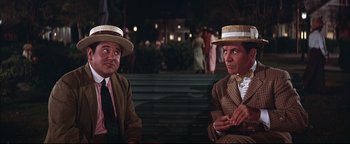 Movie still from “The Music Man” (1962), directed by Morton DaCosta – A couple of men sitting next to each other on top of a bench; Medium shot, Over the shoulder angle
