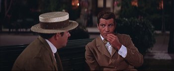 Movie still from “The Music Man” (1962), directed by Morton DaCosta – Two men sitting on a park bench one of which is eating a piece of cake; Medium shot, Over the shoulder angle