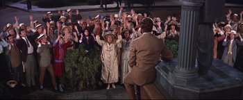 Movie still from “The Music Man” (1962), directed by Morton DaCosta – A group of people standing in front of a crowd of onlookers; Wide shot, High angle