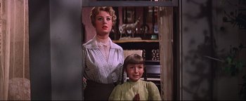 Movie still from “The Music Man” (1962), directed by Morton DaCosta – A woman standing next to a young girl in front of a piano; Medium shot, Low angle