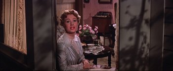 Movie still from “The Music Man” (1962), directed by Morton DaCosta – A woman sitting at a table in front of a window; Medium shot, Over the shoulder angle