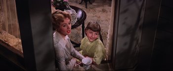 Movie still from “The Music Man” (1962), directed by Morton DaCosta – A woman sitting next to a little girl holding a coffee cup; Medium shot, High angle