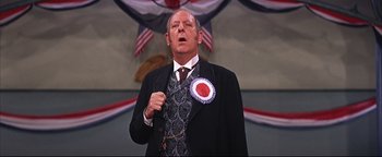 Movie still from “The Music Man” (1962), directed by Morton DaCosta – A man in a suit and tie holding a badge; Close Up shot, Low angle