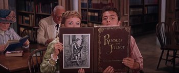 Movie still from “The Music Man” (1962), directed by Morton DaCosta – A couple of people that are holding up some books; Close Up shot, Low angle