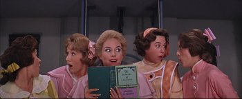 Movie still from “The Music Man” (1962), directed by Morton DaCosta – A group of three women holding books in front of a wall; Medium shot, Low angle