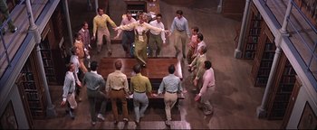 Movie still from “The Music Man” (1962), directed by Morton DaCosta – A group of men standing around a wooden table; Wide shot, High angle