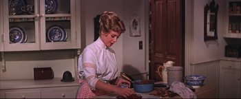 Movie still from “The Music Man” (1962), directed by Morton DaCosta – A woman in white shirt and red checkered apron in a kitchen; Medium shot, Low angle