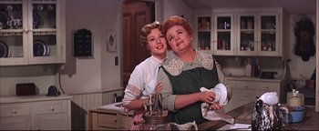 Movie still from “The Music Man” (1962), directed by Morton DaCosta – Two women are posing for a picture in a kitchen; Medium shot, Low angle