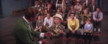 Movie still from “The Music Man” (1962), directed by Morton DaCosta – A boy in a hat is holding a french horn; Medium shot, High angle