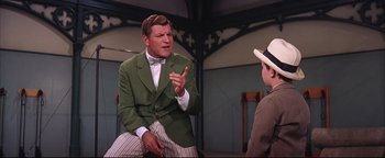 Movie still from “The Music Man” (1962), directed by Morton DaCosta – A man in a green jacket talking to a man in a white hat; Medium shot, Over the shoulder angle