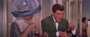 Movie still from “The Music Man” (1962), directed by Morton DaCosta – A man in a green jacket and a woman in a blue hat are sitting at a dinner table; Medium shot, Over the shoulder angle