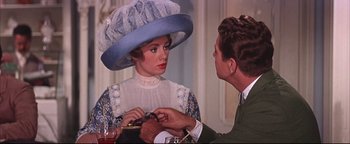 Movie still from “The Music Man” (1962), directed by Morton DaCosta – A woman wearing a blue hat is looking at a man in a green suit; Medium shot, Over the shoulder angle
