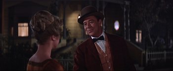 Movie still from “The Music Man” (1962), directed by Morton DaCosta – A man in a hat and a suit talking to a woman in a dress; Medium shot, Over the shoulder angle