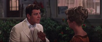 Movie still from “The Music Man” (1962), directed by Morton DaCosta – A man wearing a white suit talking to another man in front of a building; Close Up shot, Over the shoulder angle