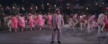 Movie still from “The Music Man” (1962), directed by Morton DaCosta – A man in a suit and tie standing in front of a group of people; Wide shot, High angle