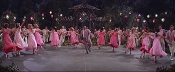 Movie still from “The Music Man” (1962), directed by Morton DaCosta – A group of people in pink dresses dancing on a stage; Wide shot, High angle
