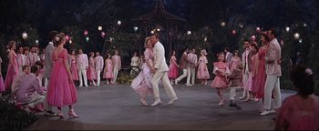 Movie still from “The Music Man” (1962), directed by Morton DaCosta – A group of people in pink outfits dancing on a stage; Wide shot, High angle