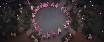 Movie still from “The Music Man” (1962), directed by Morton DaCosta – A group of women in pink dresses dancing in a circle; Extreme Wide shot, Overhead angle