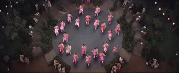 Movie still from “The Music Man” (1962), directed by Morton DaCosta – A group of women in pink dresses dancing in a circle; Extreme Wide shot, Overhead angle