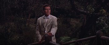 Movie still from “The Music Man” (1962), directed by Morton DaCosta – A man in a suit and bow tie standing next to a tree; Medium shot, Low angle