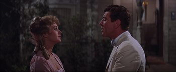 Movie still from “The Music Man” (1962), directed by Morton DaCosta – A man and a woman standing next to each other in front of a building; Close Up shot, Low angle