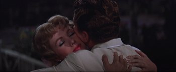 Movie still from “The Music Man” (1962), directed by Morton DaCosta – A man and a woman embracing each other in front of a dark background; Close Up shot, High angle