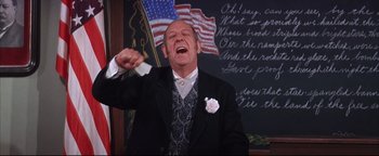 Movie still from “The Music Man” (1962), directed by Morton DaCosta – An older man wearing a suit and tie and holding a tissue in his mouth; Medium shot, Low angle