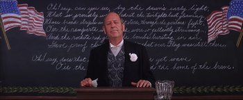 Movie still from “The Music Man” (1962), directed by Morton DaCosta – A man in a suit and tie sitting in front of a chalkboard; Medium shot, Low angle