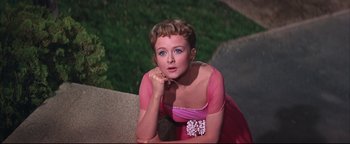 Movie still from “The Music Man” (1962), directed by Morton DaCosta – A woman in a pink dress sitting on a ledge; Close Up shot, Low angle