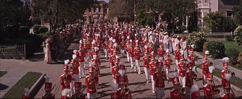Movie still from “The Music Man” (1962), directed by Morton DaCosta – A large group of people in red and white uniforms marching down a street; Extreme Wide shot, High angle