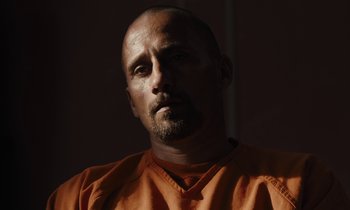 Movie still from “The Mustang” (2019), directed by Laure de Clermont-Tonnerre – A man in an orange shirt is looking at the camera; Close Up shot, Low angle