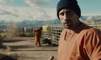 Movie still from “The Mustang” (2019), directed by Laure de Clermont-Tonnerre – A man in an orange shirt wearing a blue hat; Close Up shot, Over the shoulder angle