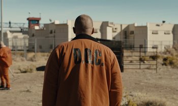 Movie still from “The Mustang” (2019), directed by Laure de Clermont-Tonnerre – A man in an orange jacket standing in front of a fence; Wide shot, Over the shoulder angle