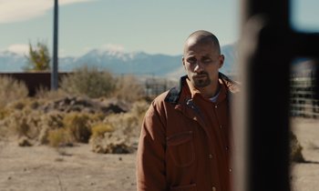 Movie still from “The Mustang” (2019), directed by Laure de Clermont-Tonnerre – A man in a brown jacket standing on a dirt field; Close Up shot, Over the shoulder angle