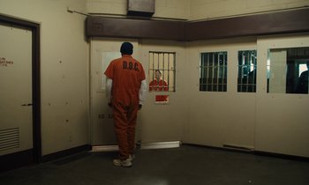 Movie still from “The Mustang” (2019), directed by Laure de Clermont-Tonnerre – A man in an orange jumpsuit standing in a jail cell; Wide shot, High angle