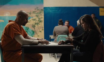 Movie still from “The Mustang” (2019), directed by Laure de Clermont-Tonnerre – Two people sitting at a table in a room; Medium shot, Over the shoulder angle