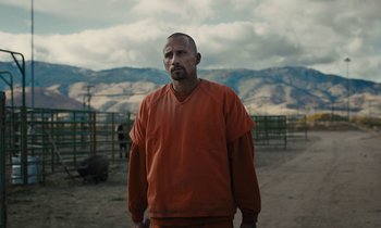 Movie still from “The Mustang” (2019), directed by Laure de Clermont-Tonnerre – A man in an orange shirt standing in a dirt field; Medium shot, Low angle
