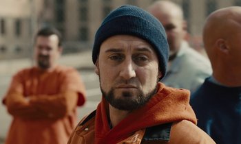 Movie still from “The Mustang” (2019), directed by Laure de Clermont-Tonnerre – A person wearing an orange jacket and a blue hat; Close Up shot, Over the shoulder angle