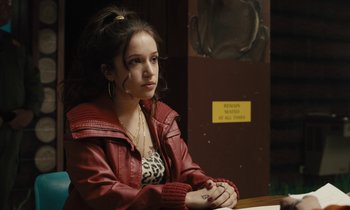 Movie still from “The Mustang” (2019), directed by Laure de Clermont-Tonnerre – A young woman sitting at a table in front of a sign; Medium shot, Over the shoulder angle