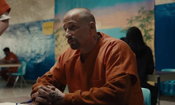 Movie still from “The Mustang” (2019), directed by Laure de Clermont-Tonnerre – A man in an orange shirt is sitting in a room; Medium shot, Over the shoulder angle