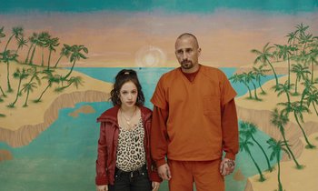 Movie still from “The Mustang” (2019), directed by Laure de Clermont-Tonnerre – A man and a woman standing next to each other in front of a painting; Medium shot, Low angle